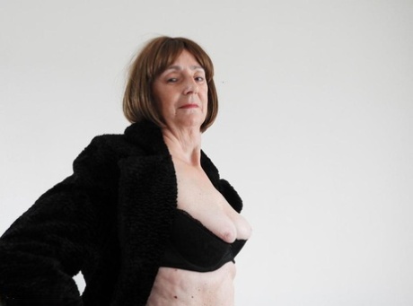 Old woman in leather boots and black 3 piece lingerie strips naked on sofa